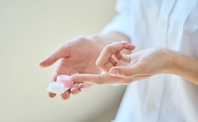Hands holding a contact lens case and balancing a lens on a fingertip